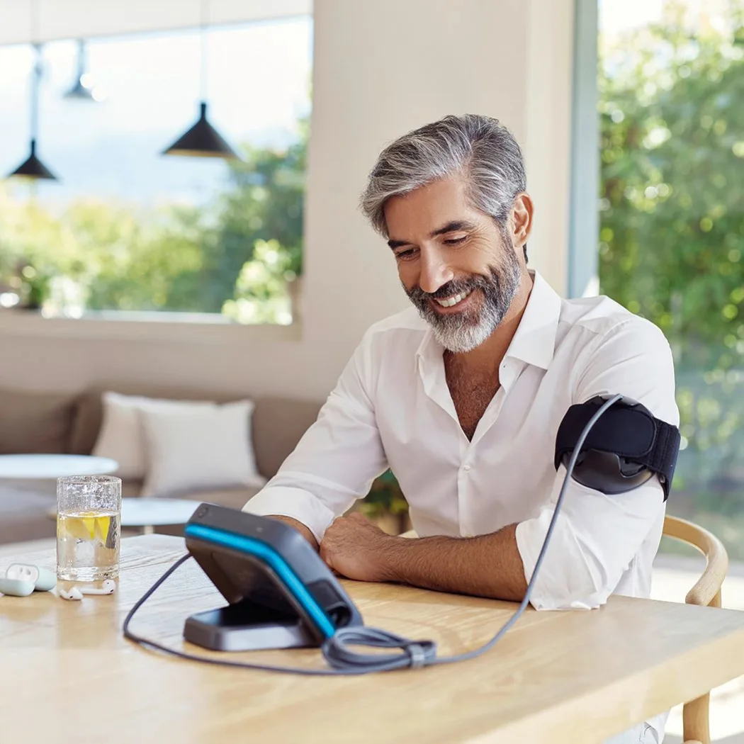 Mann sitzt lächelnd am Tisch, am Oberarm die BEMER Applikatorschlaufe, daneben das Bediengerät