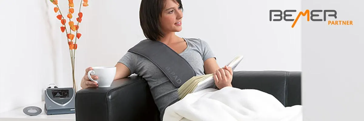 Frau liest auf dem Sofa, neben ihr das BEMER Gerät